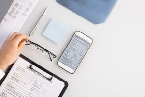 Flatlay of hand of doctor putting eyeglasses on table by medical history form