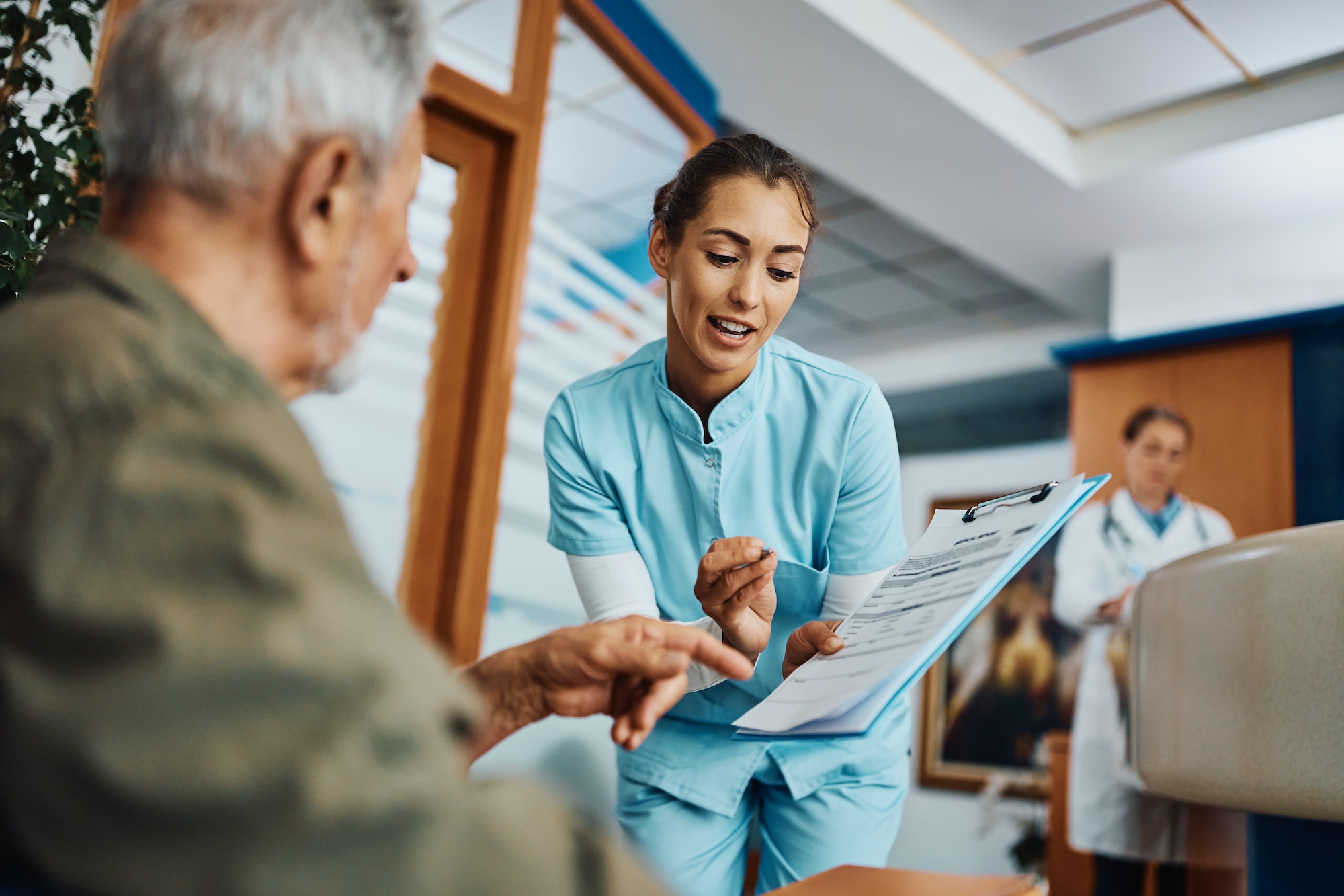 Young nurse assisting senior man in filling paperwork at doctor's office.