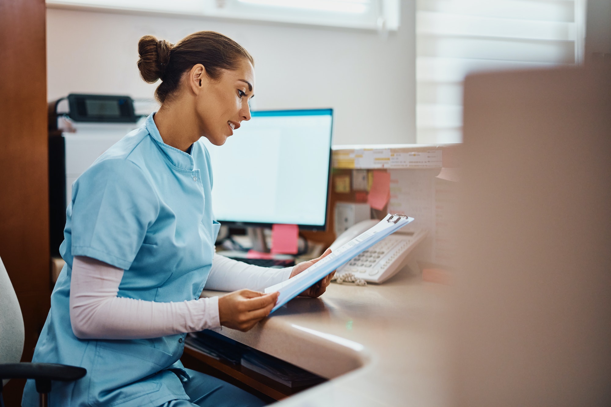 Young nurse going through medical records at reception desk in the hospital.